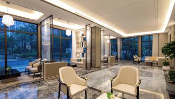 A modern hotel lobby with a marble floor, seating areas, and large windows offering a view of the outdoors.