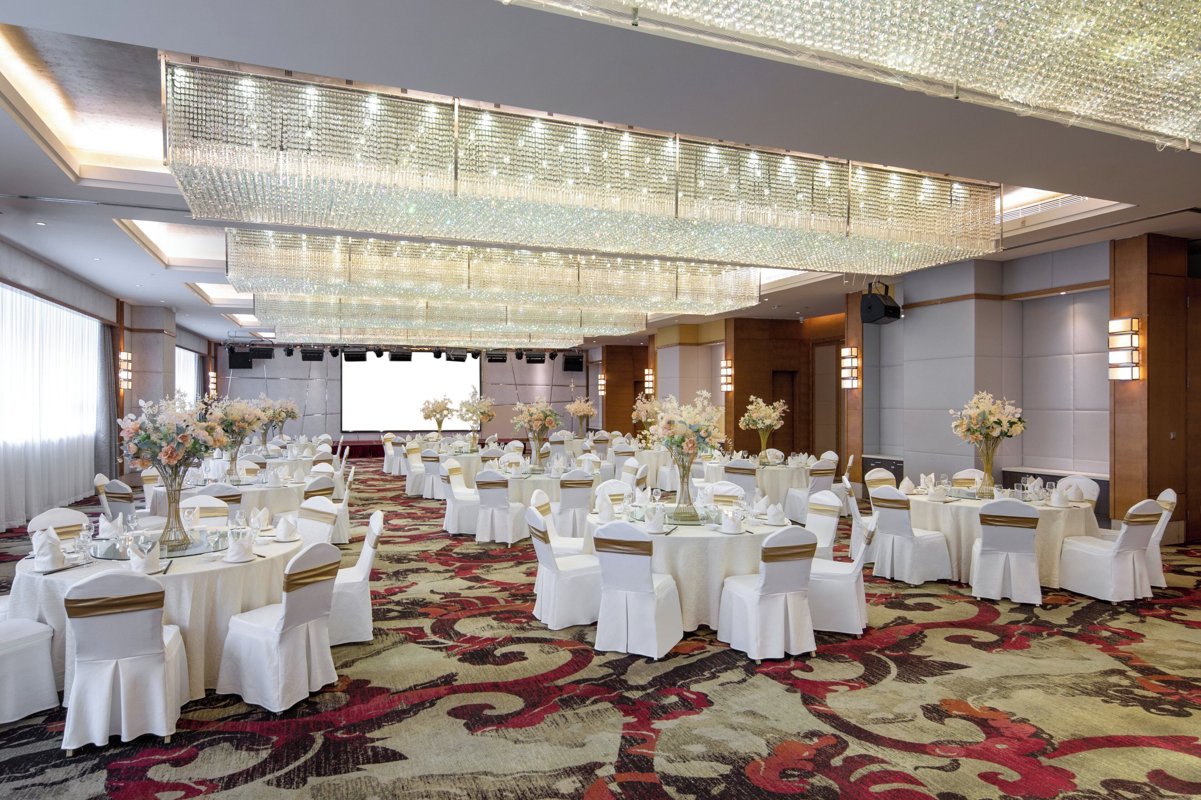 Un salón de banquetes con mesas redondas, sillas blancas y centros de mesa florales.
