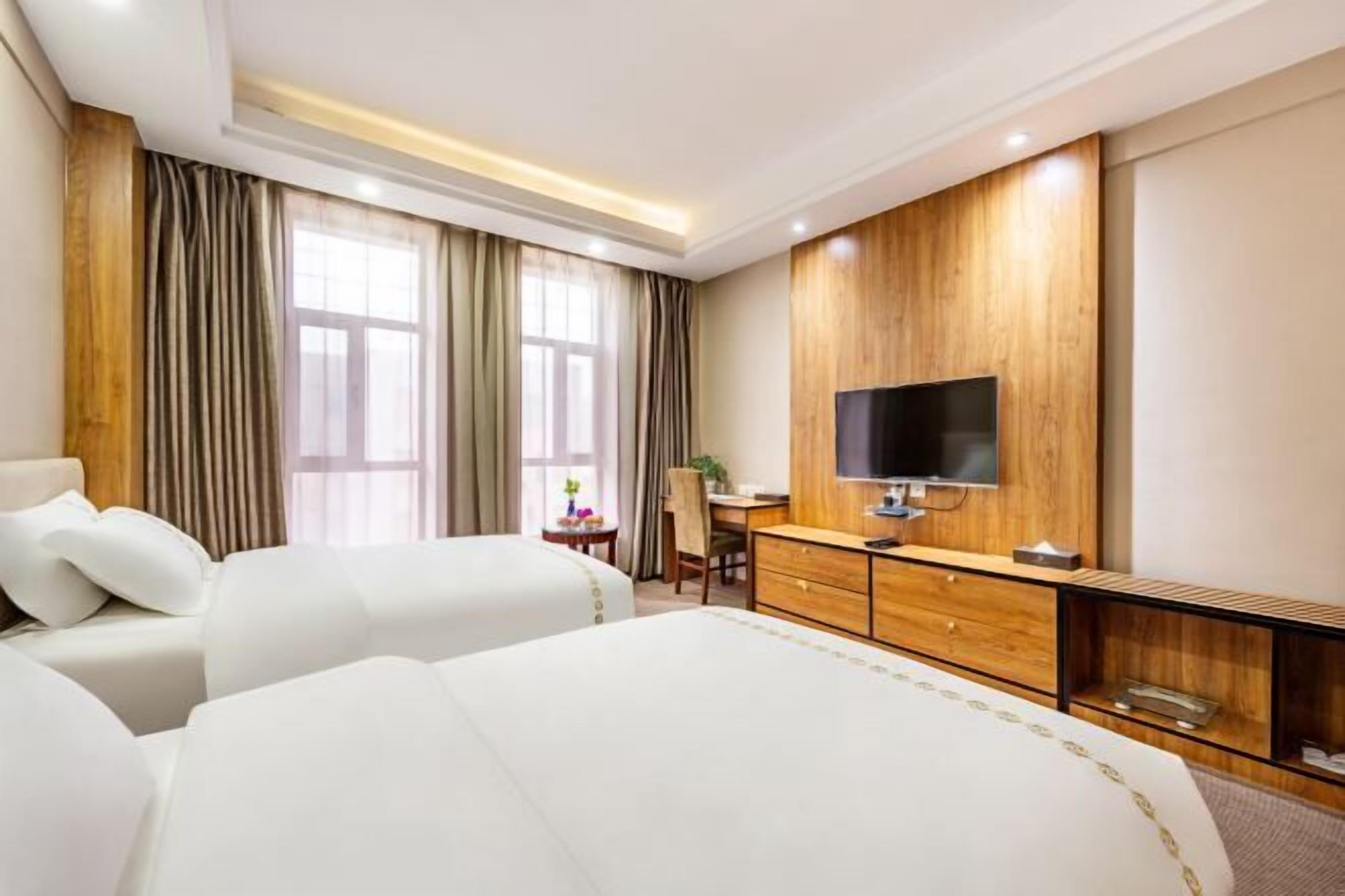 A hotel room with two beds, a wooden dresser, a TV, and a desk with a chair.