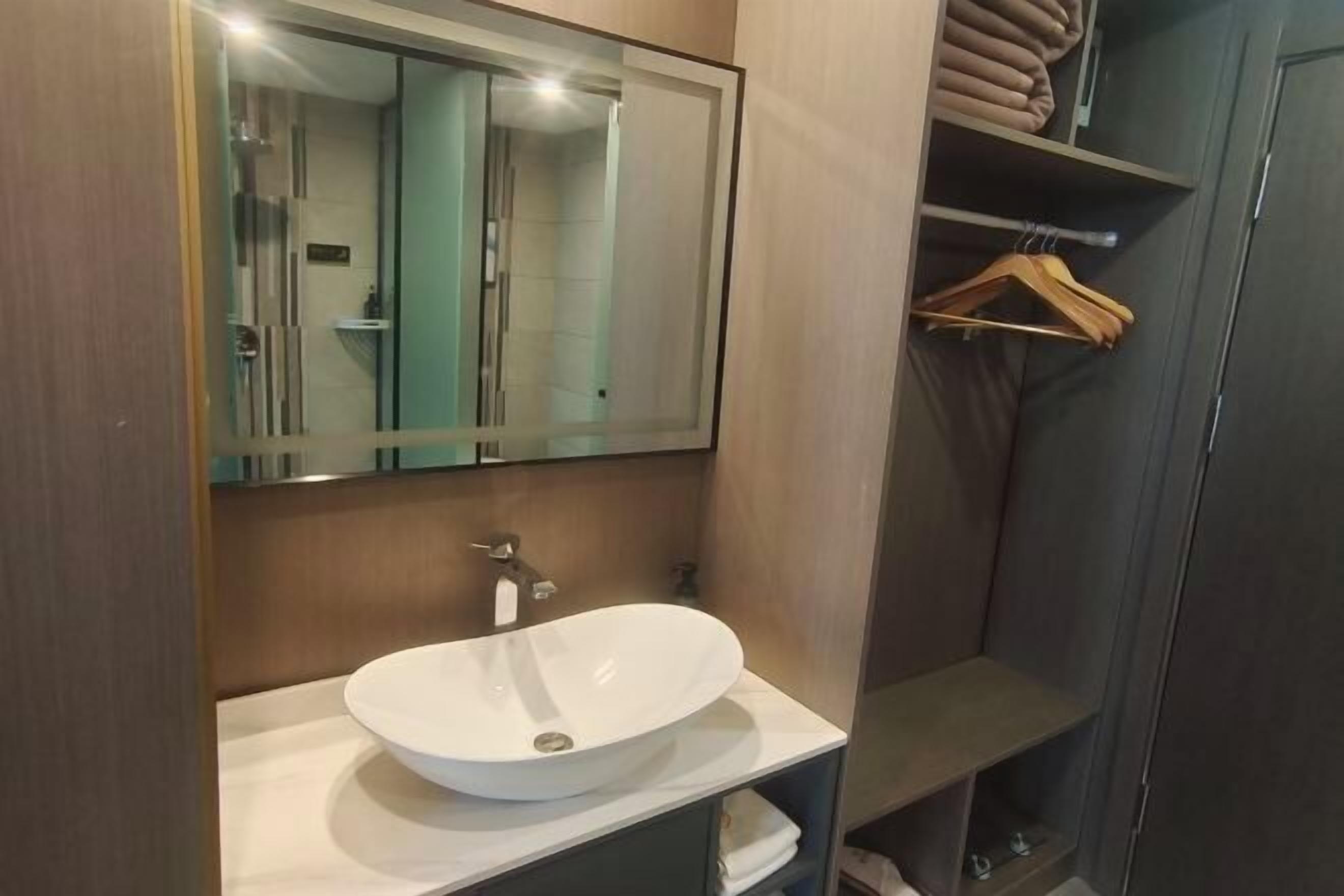 Un baño moderno con un espejo grande, un lavamanos blanco tipo recipiente y un mueble de tocador de madera.