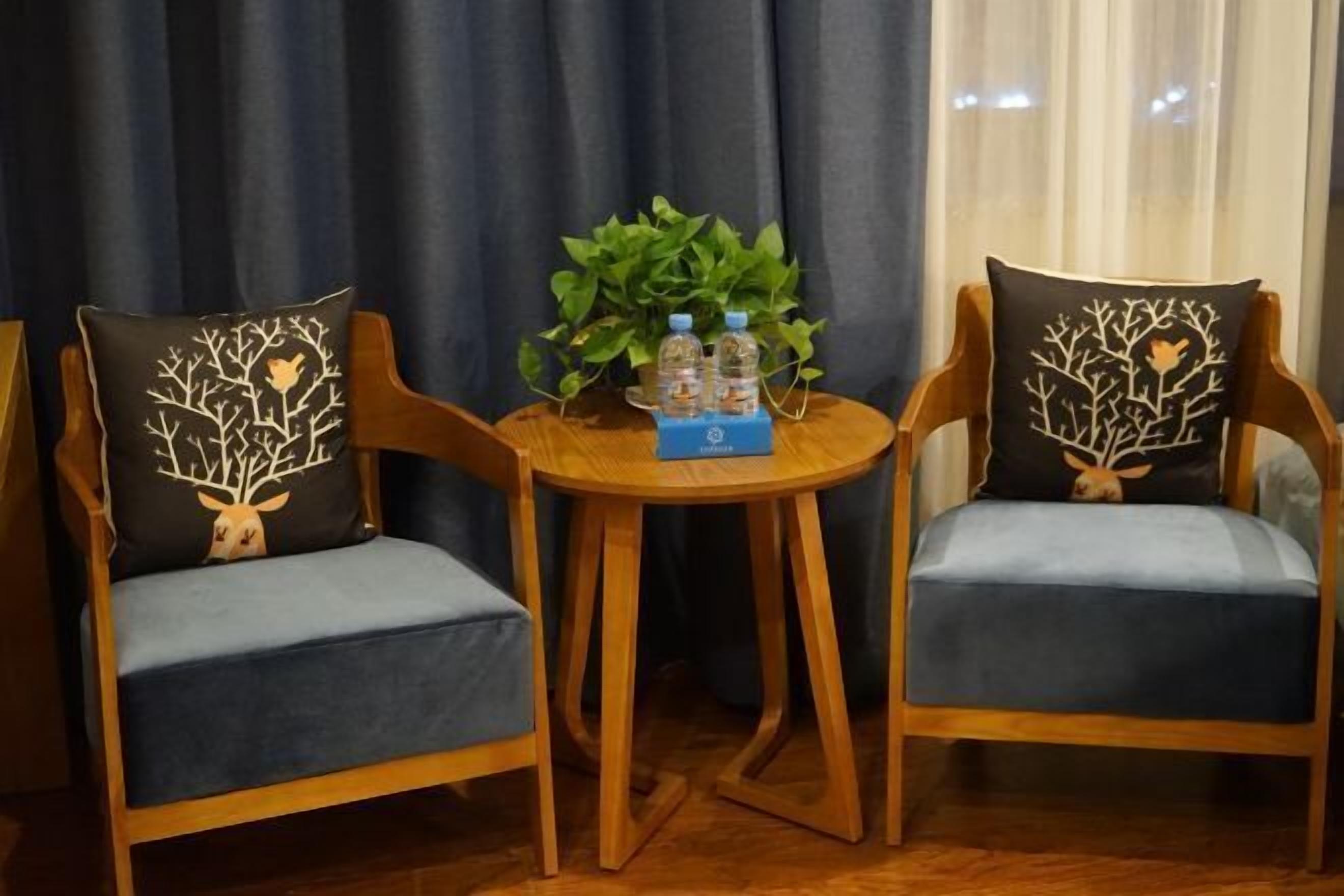 Two wooden chairs with matching cushions, a small wooden table with a plant and water bottles, and a curtain backdrop.