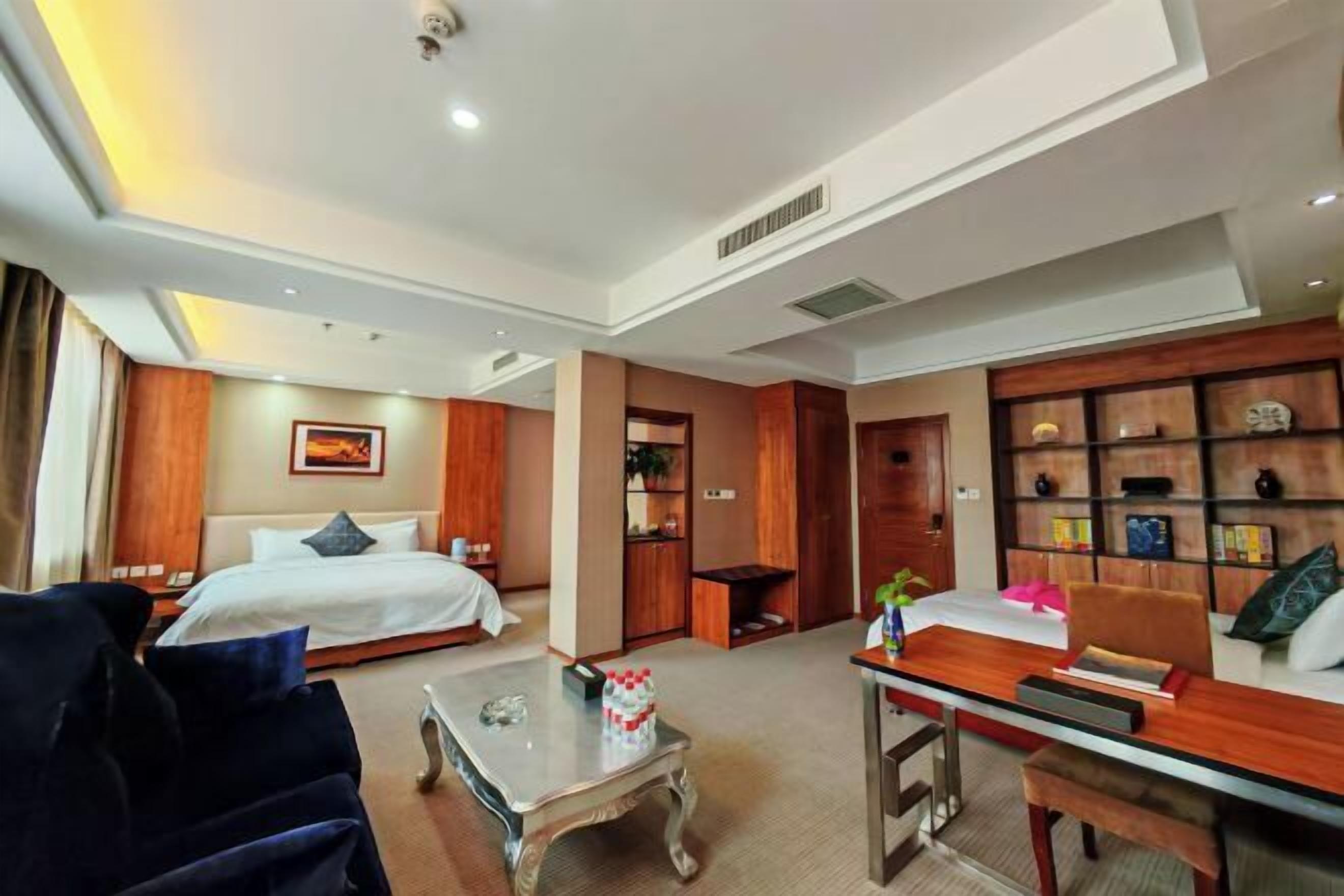 A hotel room with a bed, a desk, a chair, a coffee table, and a bookshelf.