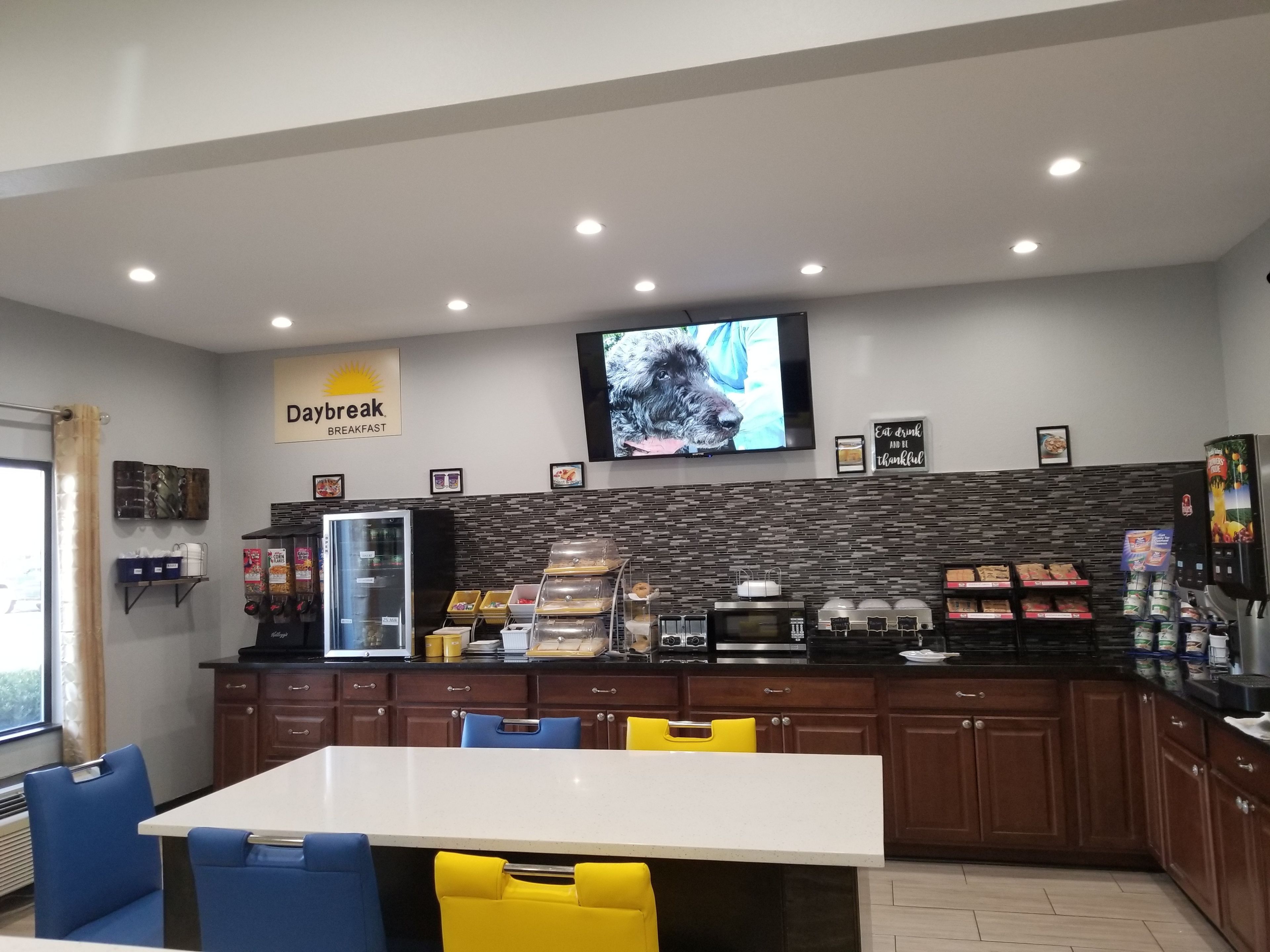 Ein Frühstücksrestaurant namens Daybreak mit einer Theke, Sitzbereich und einem Bildschirm, auf dem ein Hund zu sehen ist.