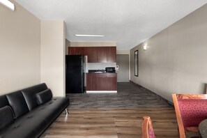 A modern living room with a black leather sofa, a wooden floor, and a kitchen area in the background. - Days Inn by Wyndham Greenville South/Mauldin (Mauldin)