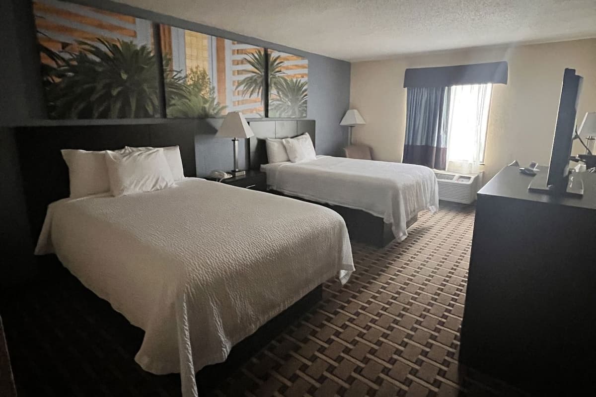 Habitación de hotel con dos camas, un escritorio, una lámpara y una ventana con cortinas.