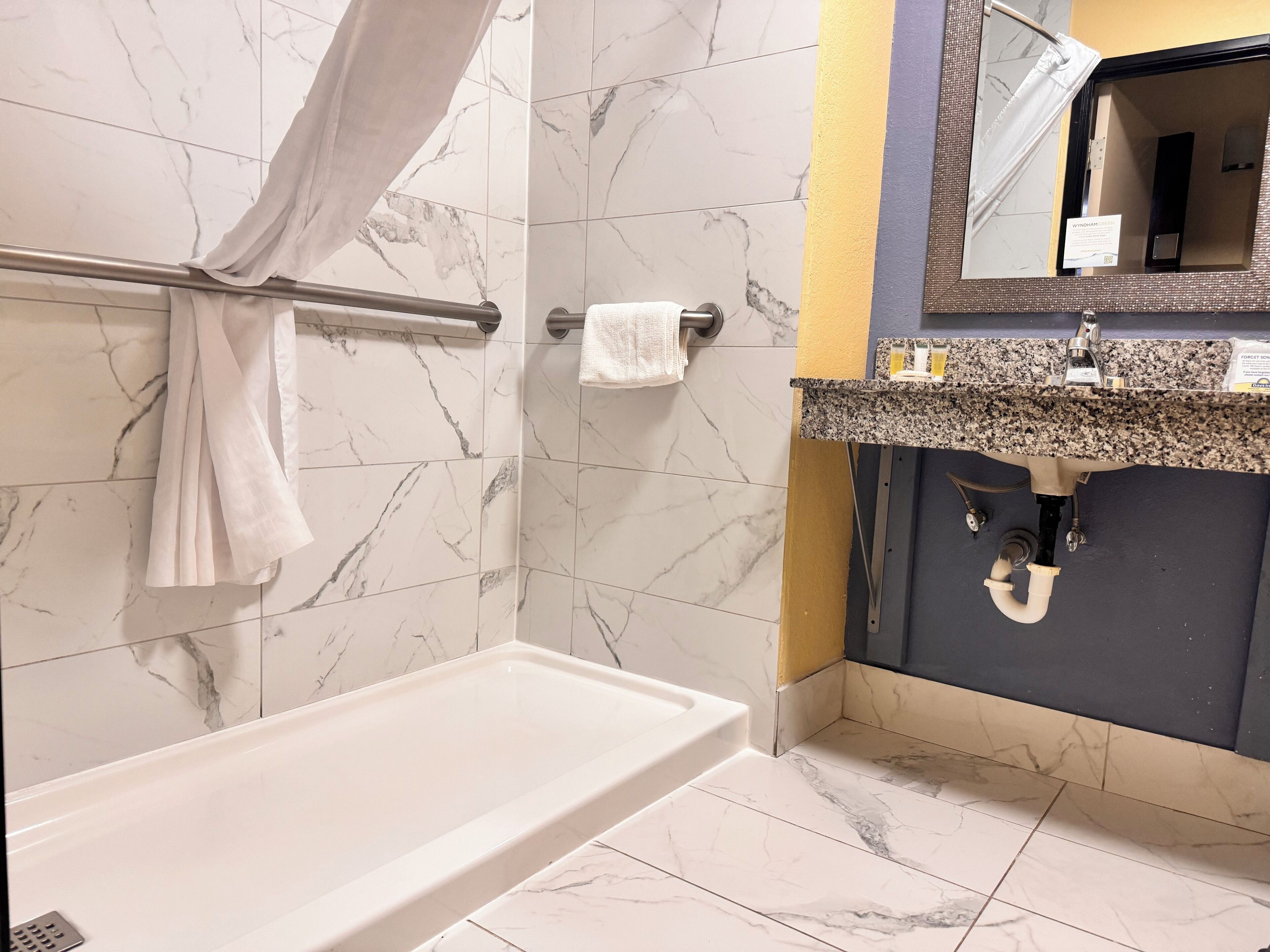 A bathroom with a bathtub, a towel rack, a sink with a granite countertop, and a mirror.