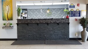 A reception desk with a stone facade, a peacock wall decoration, and a large potted plant. - Days Inn by Wyndham Greenville South/Mauldin (Mauldin)