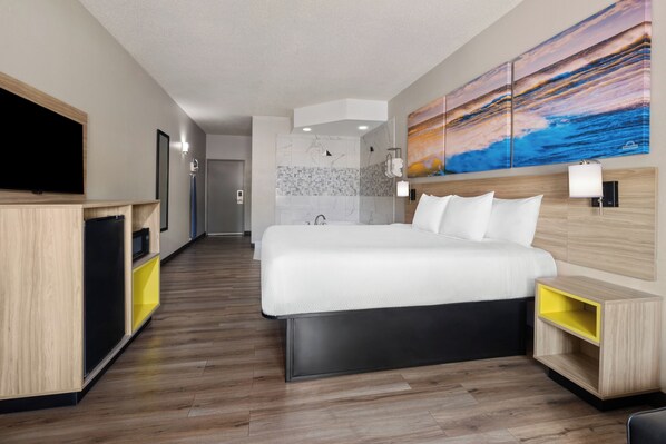 A modern hotel room with a large bed, a TV, a bathroom with a shower, and a painting on the wall.