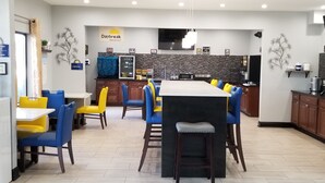 A spacious dining area with a central table and chairs, a kitchen in the background, and a sign indicating a breakfast area. - Days Inn by Wyndham Greenville South/Mauldin (Mauldin)