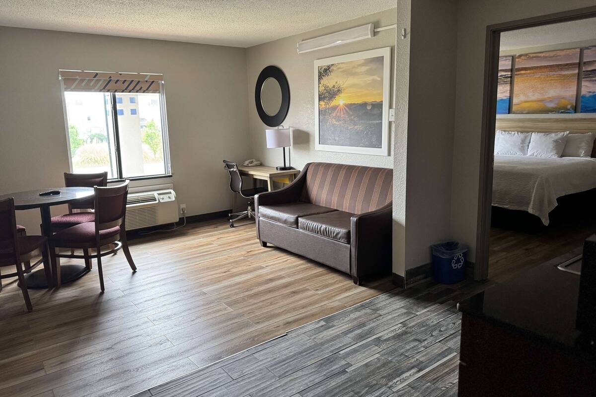 Habitación de hotel con piso de madera, un sofá, un escritorio con silla, una cama, una ventana con vista al exterior y un cuadro en la pared.