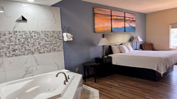 A modern hotel room with a large bed, a separate bathroom with a bathtub, a nightstand, a lamp, and a wall-mounted artwork. - Days Inn by Wyndham Greenville South/Mauldin (Mauldin)