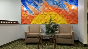 A reception area with two beige armchairs, a glass-top table, and a vibrant geometric wall art. - Days Inn by Wyndham Greenville South/Mauldin (Mauldin)