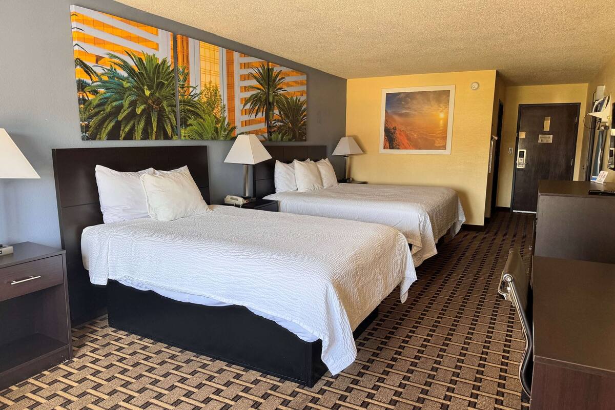 Habitación de hotel con dos camas, alfombra estampada, un cuadro de palmeras y una puerta con un letrero.