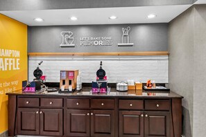 A bakery counter with waffle makers, a coffee machine, and waffle batter boxes.