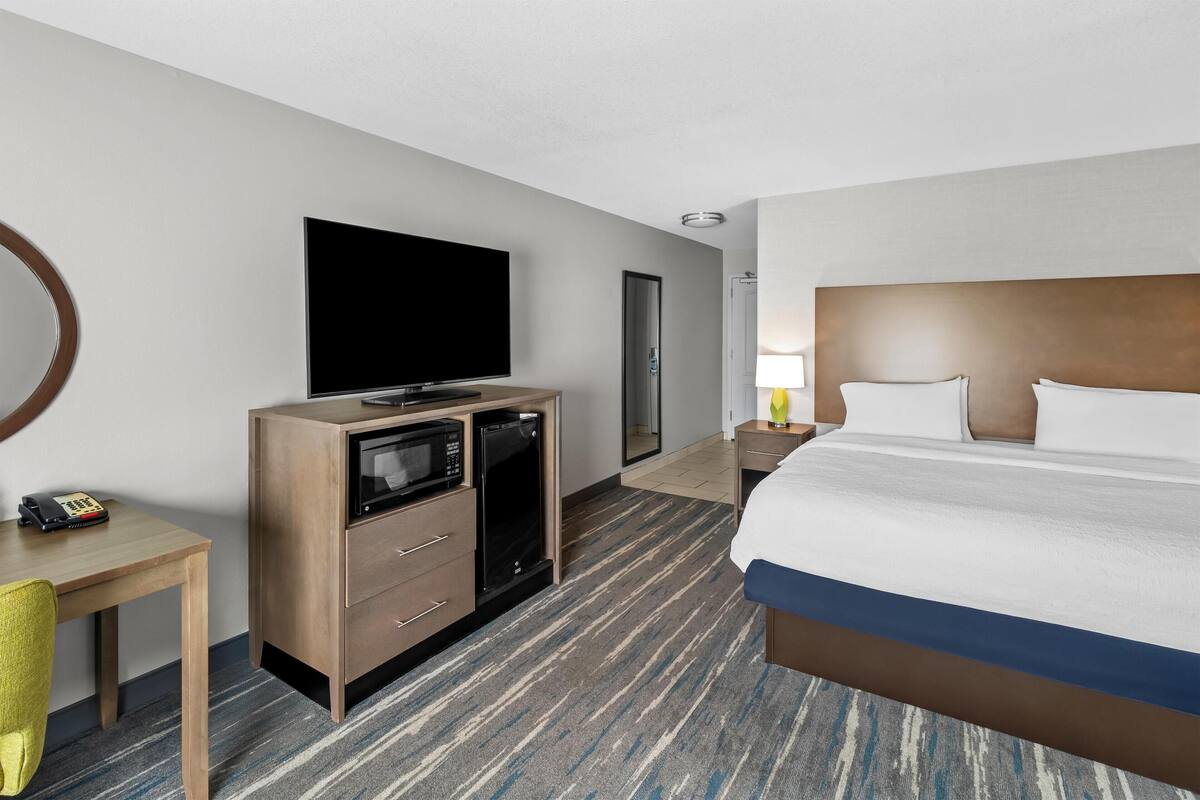 A hotel room with a bed, a television, a desk with a telephone, and a microwave.