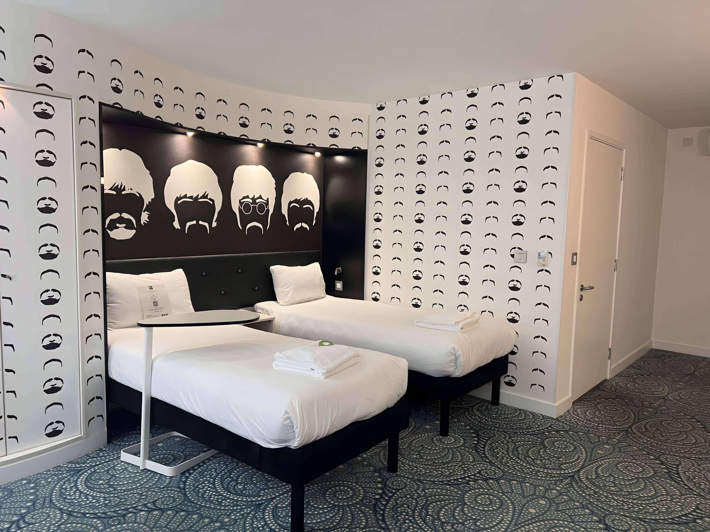 A hotel room with a bed, two bedside tables, a headboard with a unique design, patterned wallpaper, and a door.
