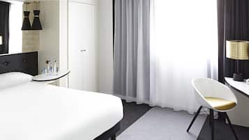 Una habitación de hotel con cama, escritorio, silla, espejo y ventana con cortinas.