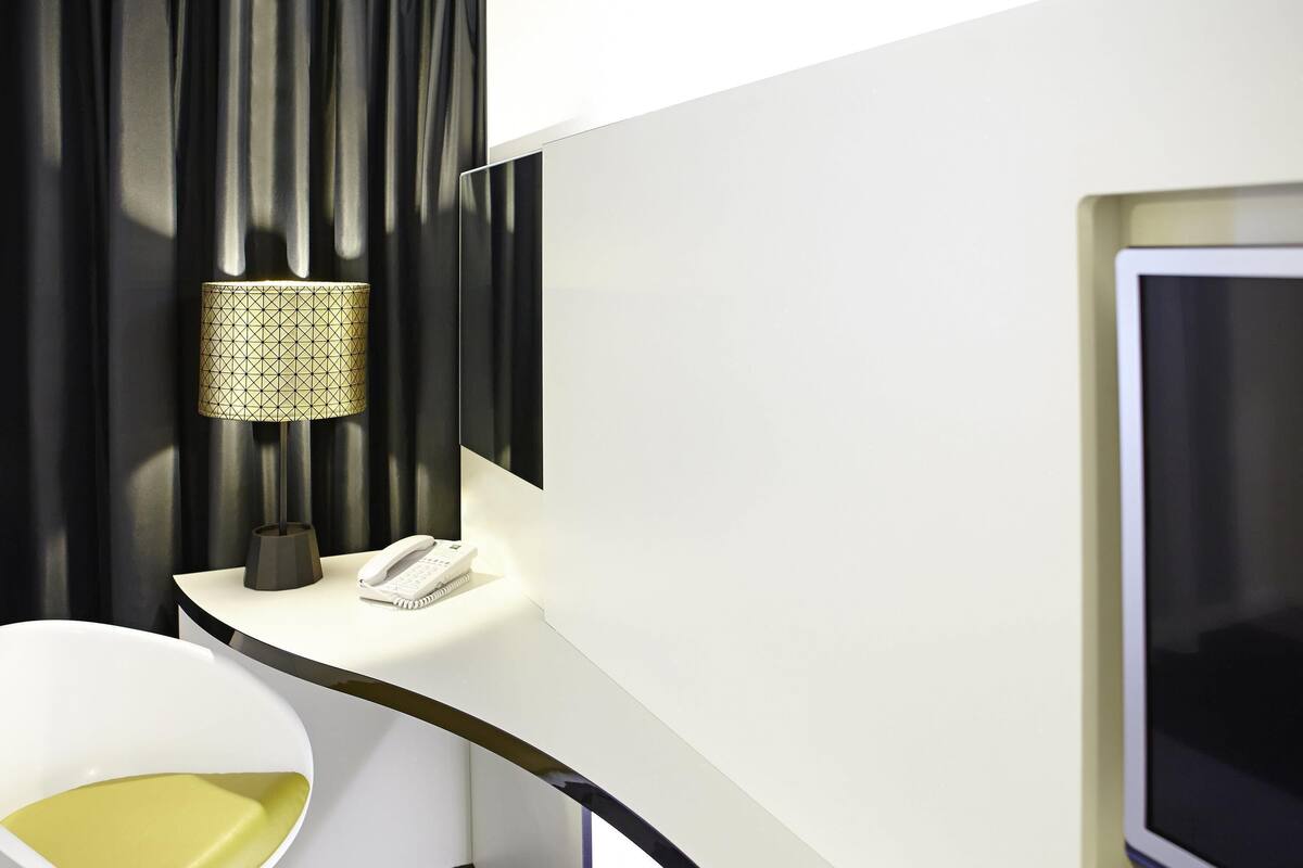 A hotel room with a desk, a telephone, a lamp, a chair, and a television.