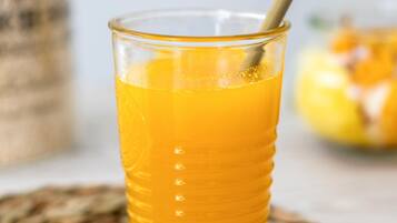 Un vaso alto de jugo de naranja con pajita, sobre un posavasos tejido.