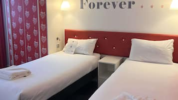 A hotel room with two single beds, a red headboard, white bedding, a bedside table, and a wall with the word "Forever" and strawberry patterns.