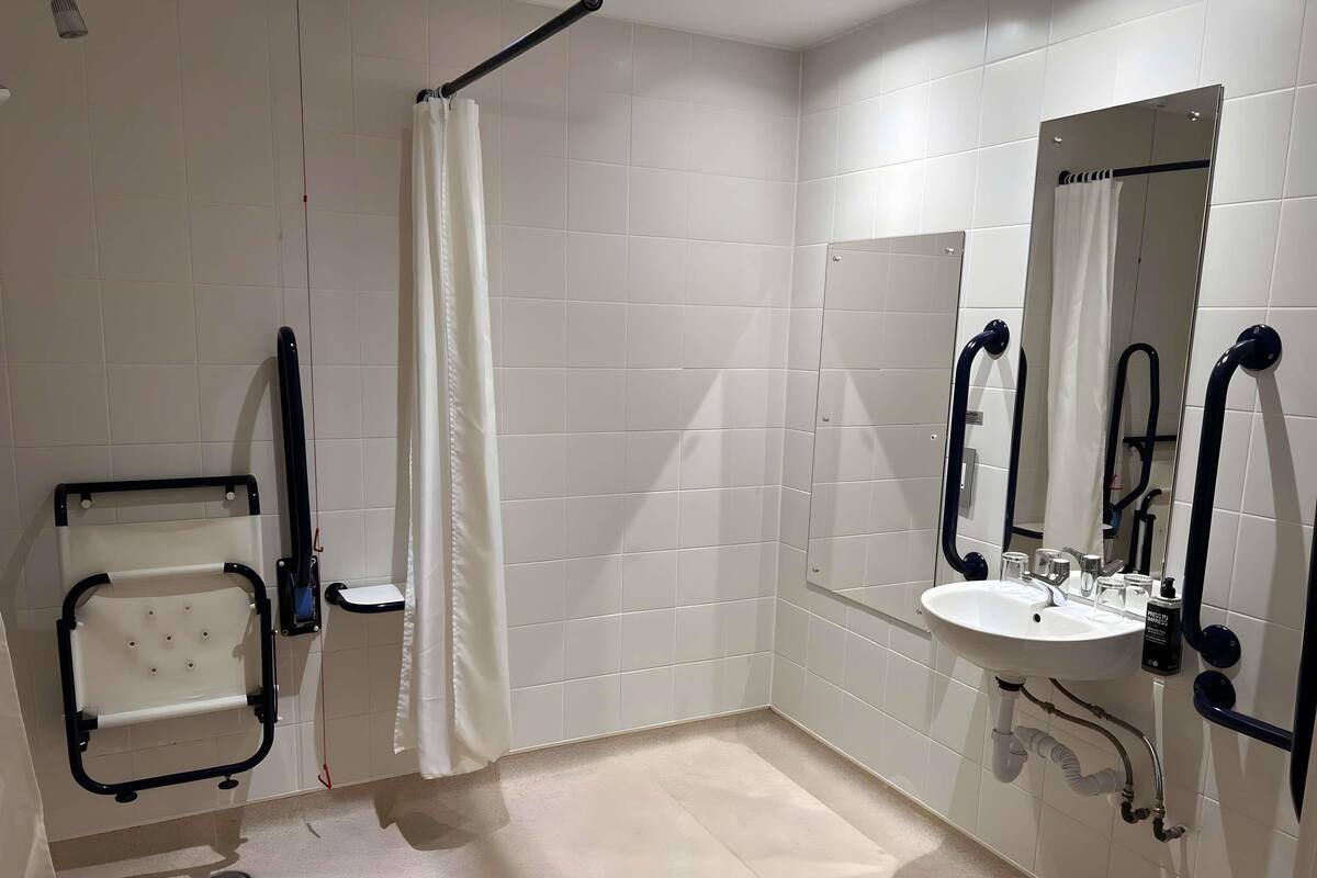 A bathroom with a white sink, mirror, toilet, shower curtain, and grab bars.