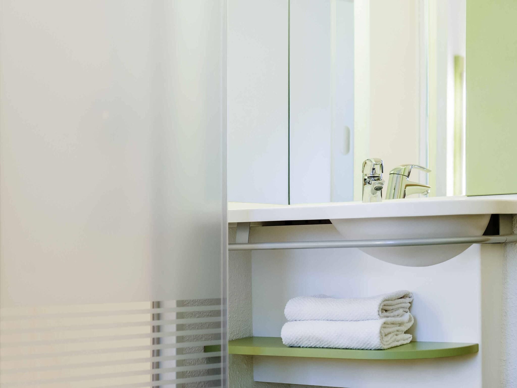 A bathroom with a white sink, a mirror, and a green shelf with folded towels.