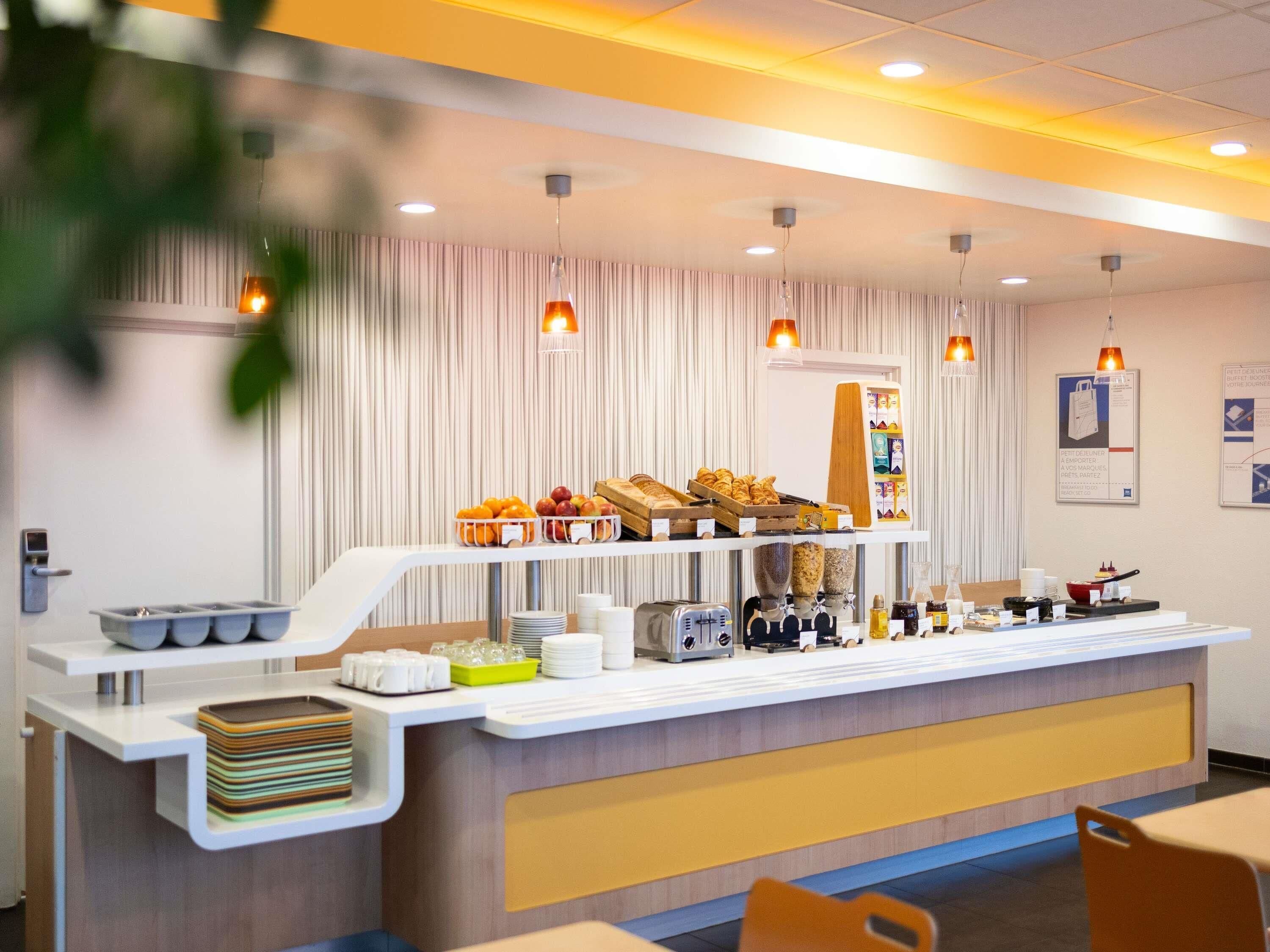 A breakfast bar with various food items, a coffee machine, and a fruit display.