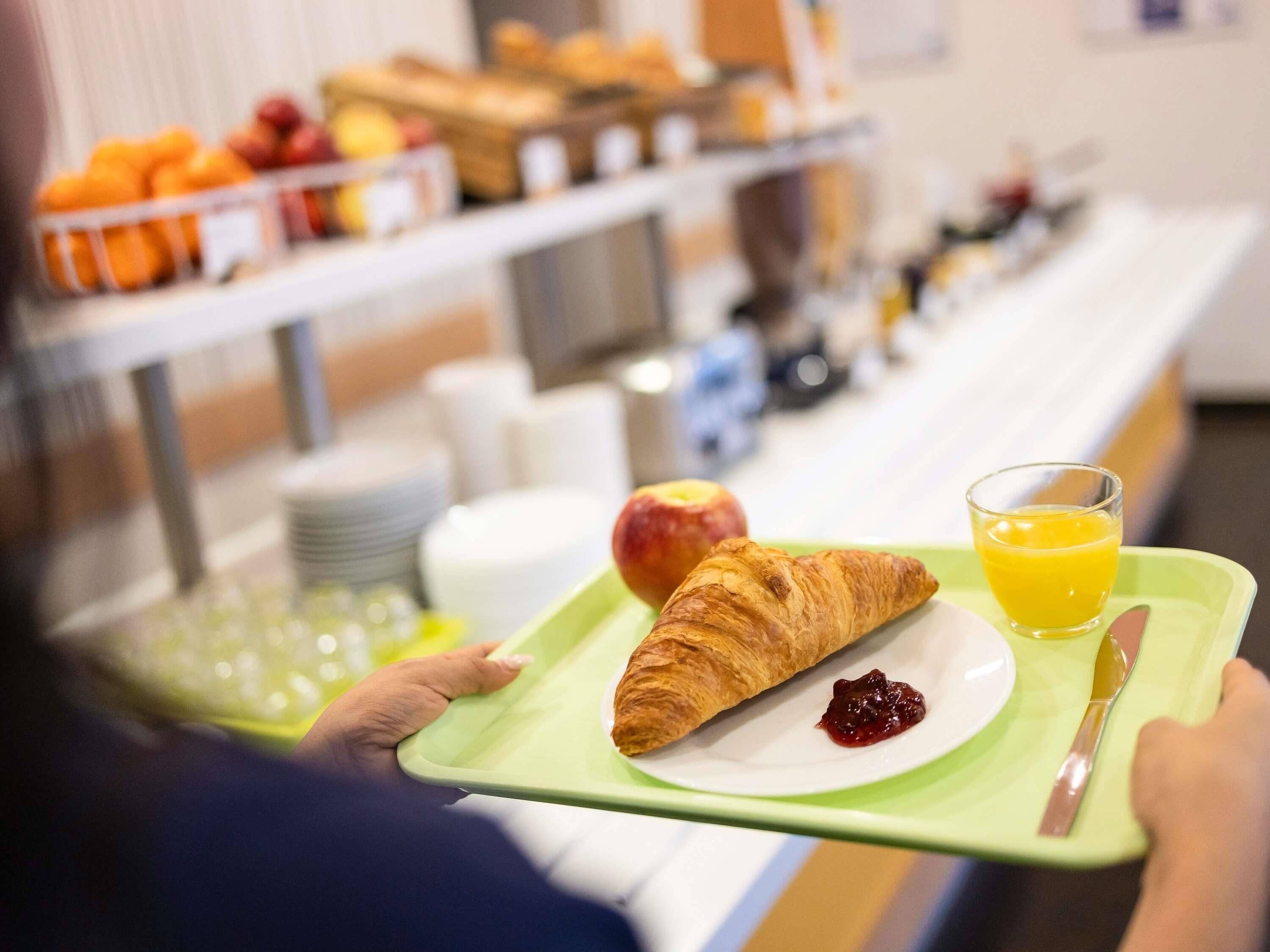 A tray with a croissant, apple, and orange juice.
