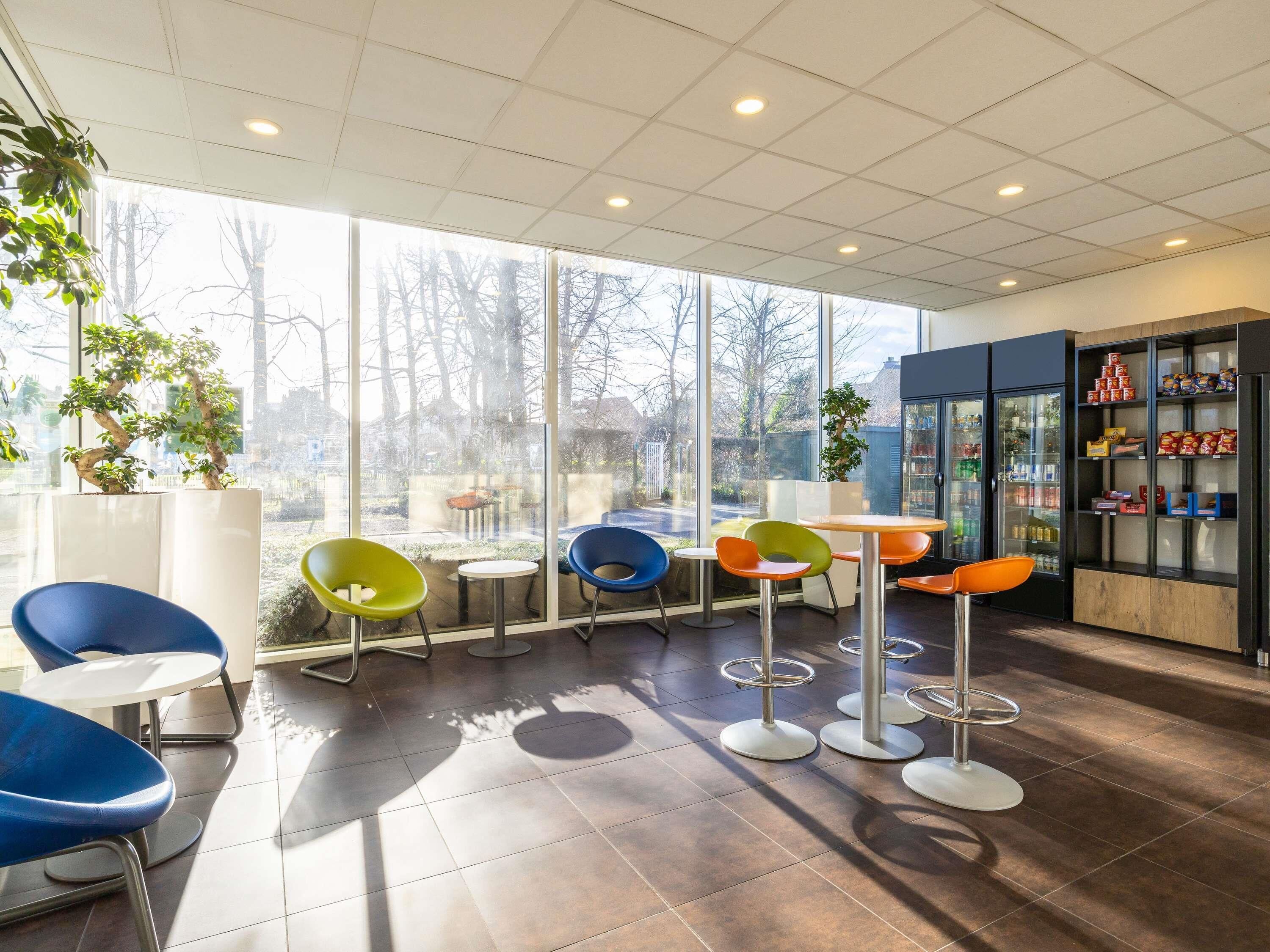 A modern cafe with large windows, colorful chairs, and a beverage display.