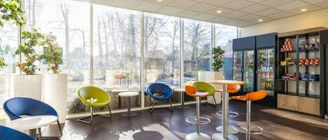 Una cafetería moderna con ventanas amplias, sillas coloridas y una presentación de bebidas.