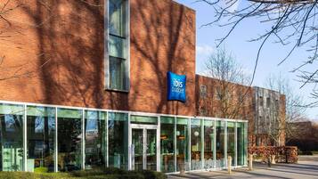 Een modern gebouw met een glazen gevel, een bord waarop 'ibis budget' staat, en een heldere lucht.