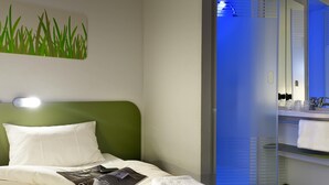 Habitación de hotel con cama, una revista, una toalla, luz de noche y espejo de baño.