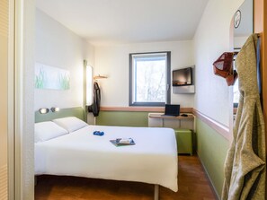 A compact hotel room with a bed, a desk with a laptop, a TV, and a window.