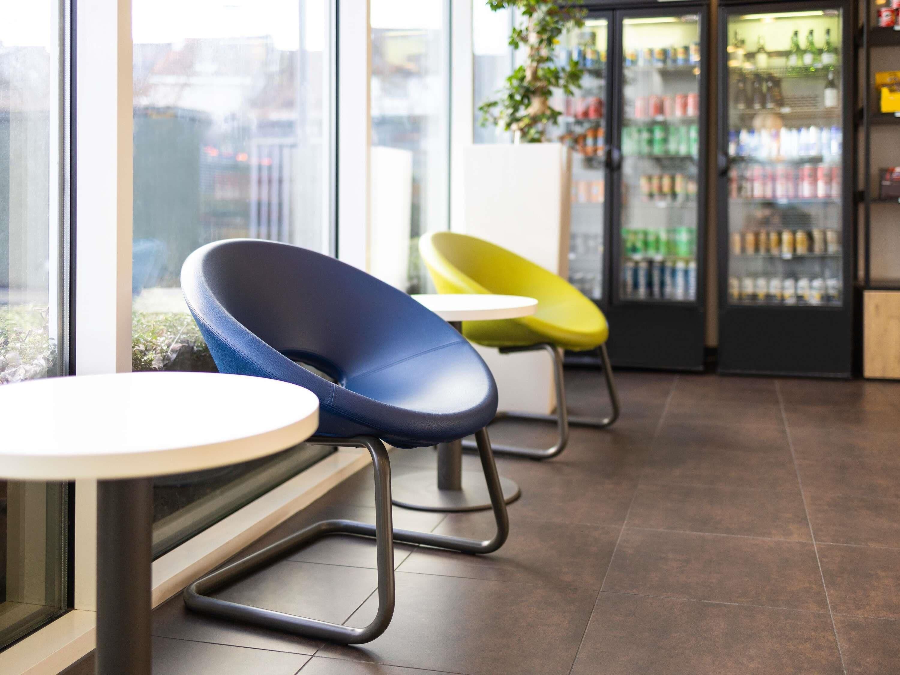 Un interior moderno con dos sillas, una mesa y un refrigerador lleno de bebidas.