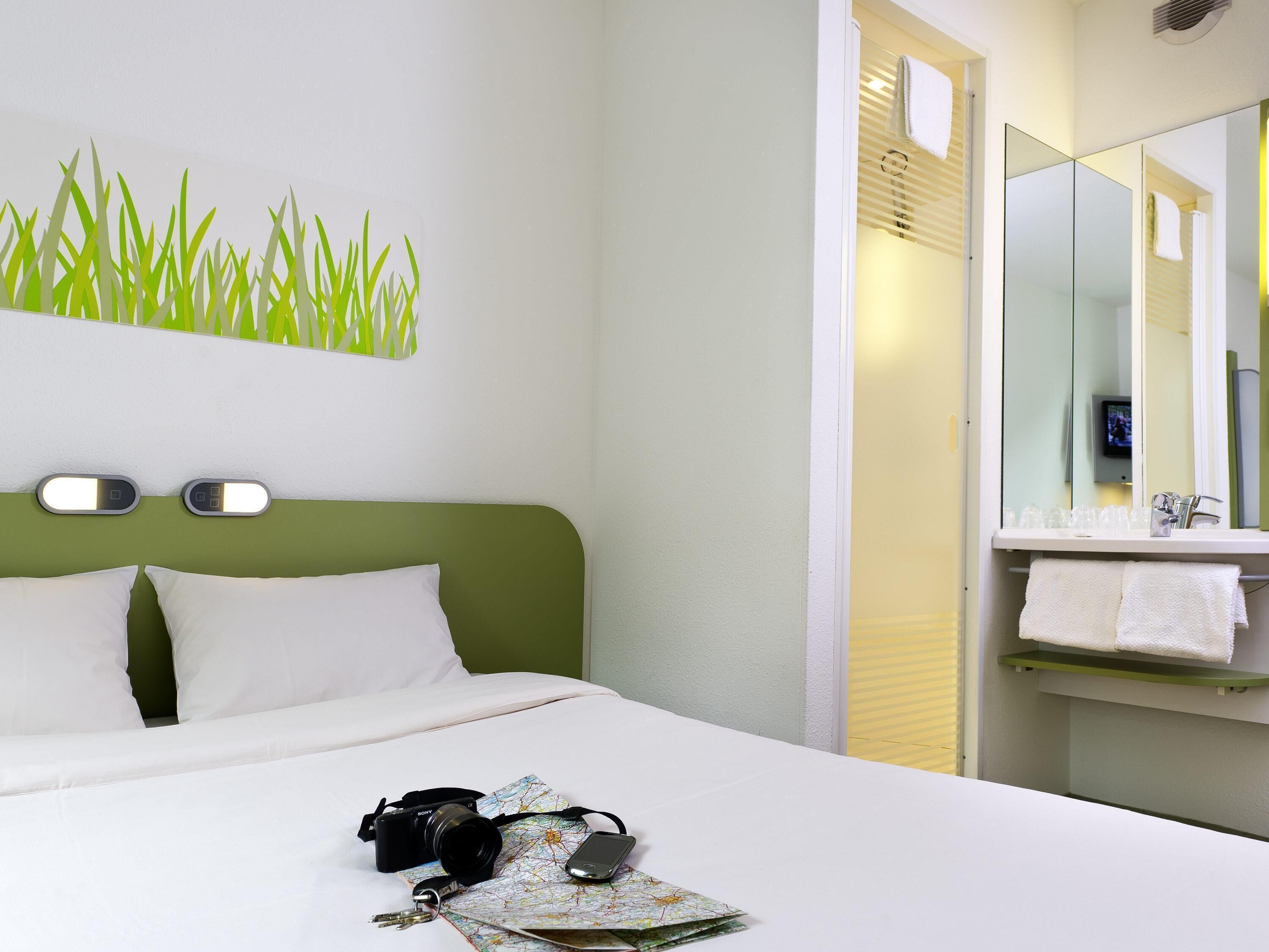 A hotel room with a bed, a map, a camera, and a bathroom with a mirror and towel rack.