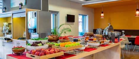 Comedor moderno de hotel con barra de buffet, que incluye diversos alimentos y una estación de café.