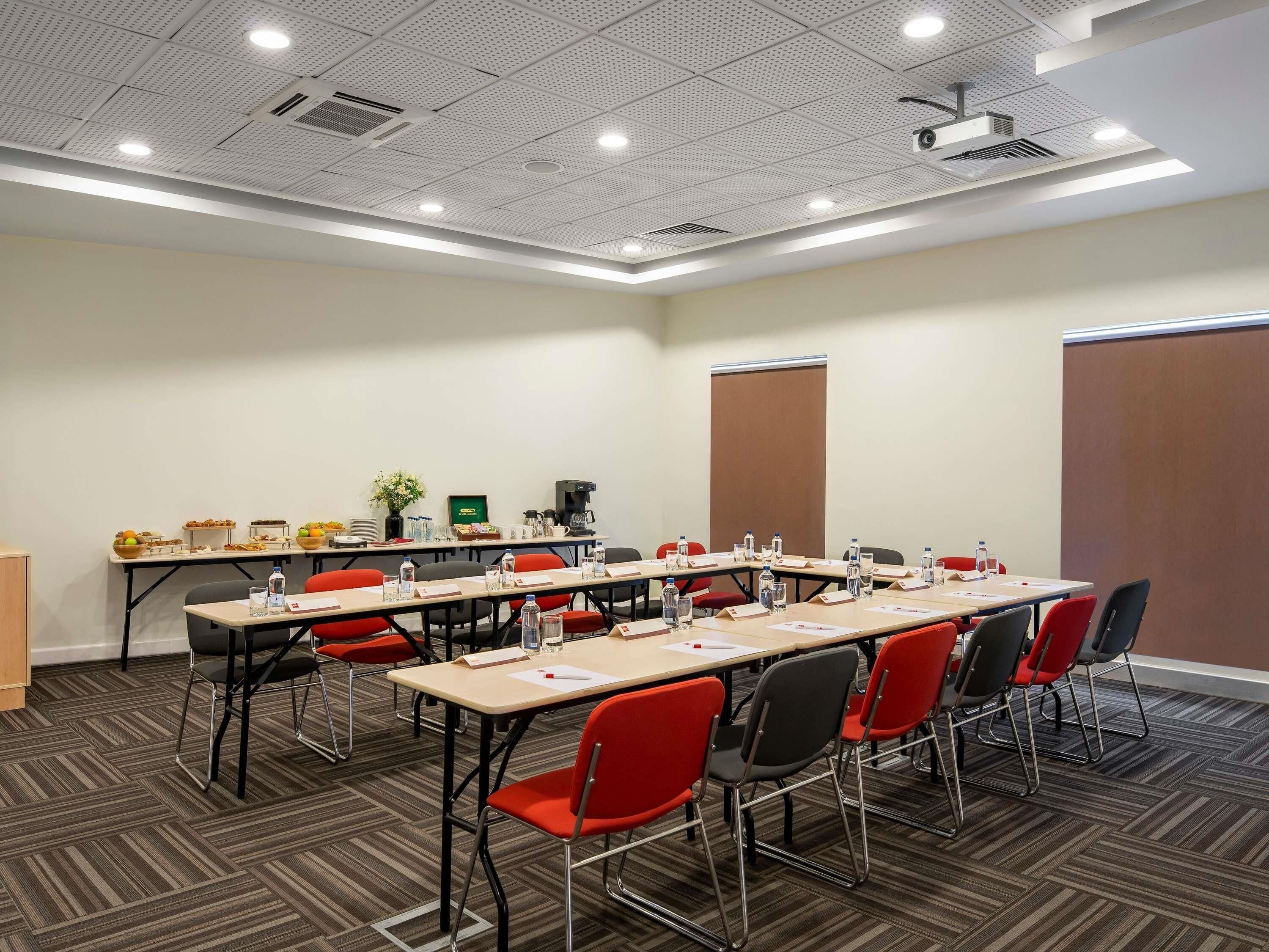 A conference room with a long table, red and black chairs, a projector, and a whiteboard.