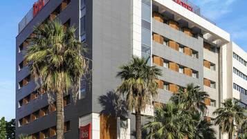 A modern hotel building with multiple floors, large windows, and palm trees in front.