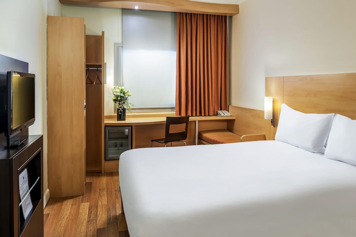A hotel room with a bed, a desk, a chair, a television, and a wardrobe.