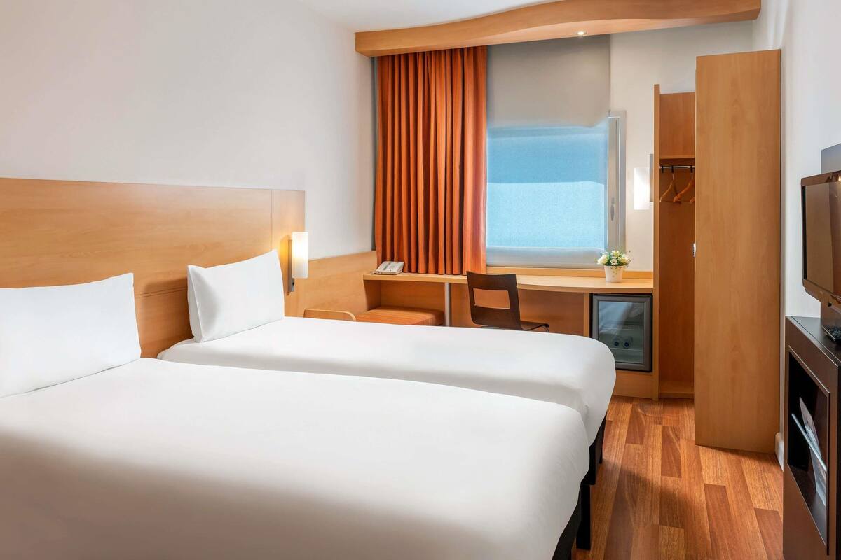 A hotel room with two beds, a desk, a chair, a television, and a wardrobe.