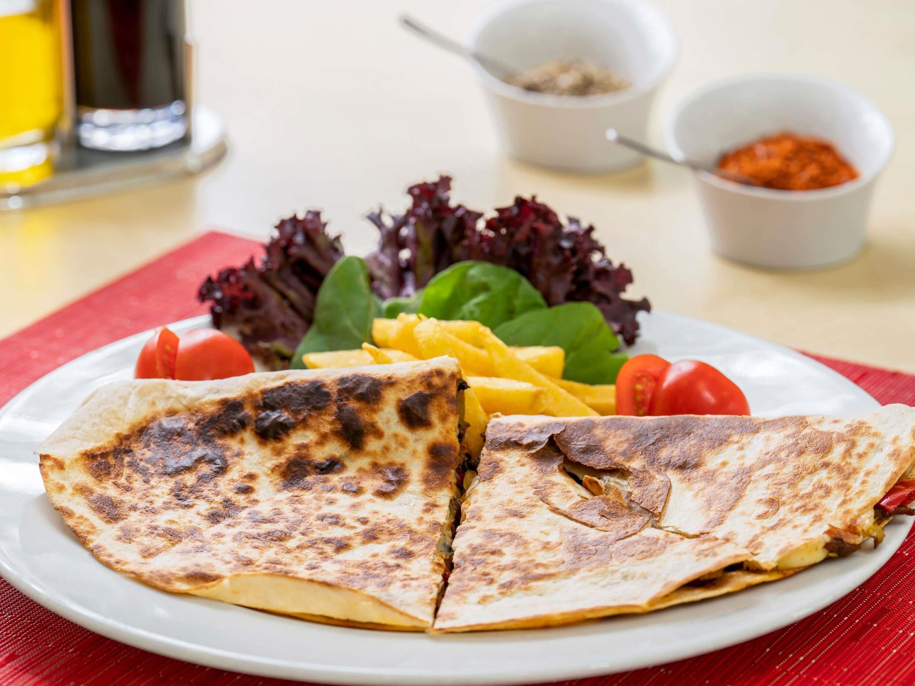 Une assiette contenant une quesadilla, une salade et des tranches de mangue.