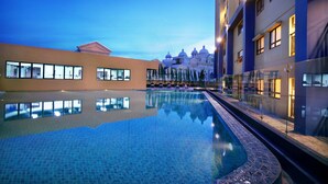 A swimming pool with a clear reflection, surrounded by modern buildings with large windows and a poolside area. - Atria Residences Gading Serpong (Gading Serpong)