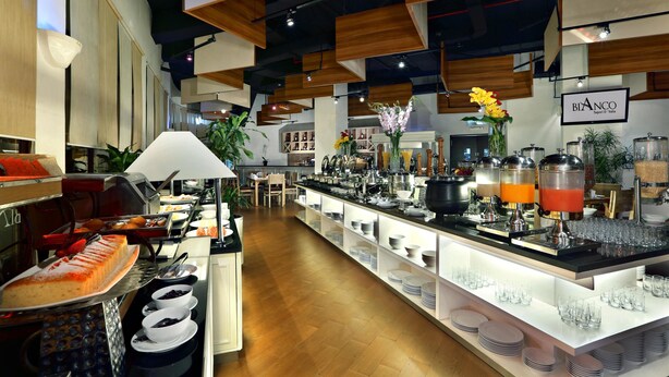 A modern hotel lobby with a long reception counter, a coffee station, and a dining area with tables and chairs. - Atria Residences Gading Serpong (Gading Serpong)