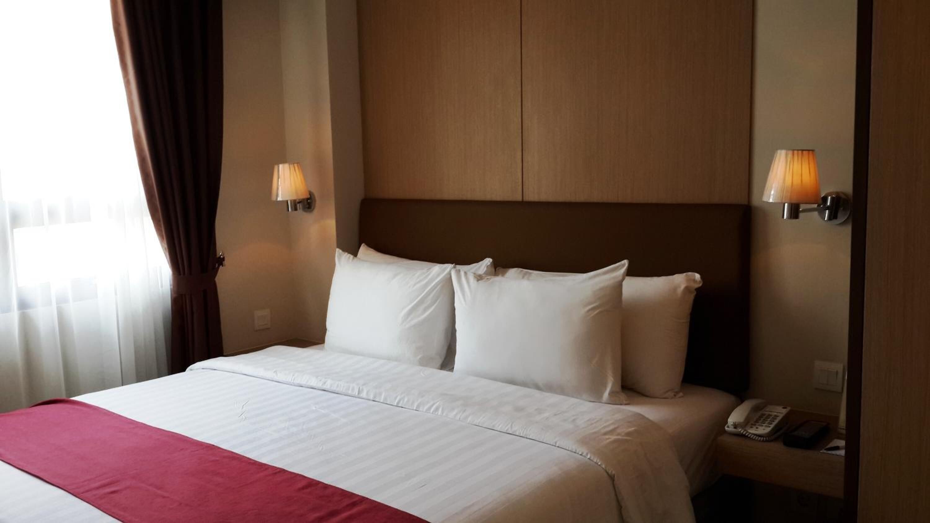Une chambre d’hôtel avec un grand lit, deux lampes de chevet, un téléphone et un plaid rouge.