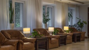 A room with six leather sofas arranged in a row, each with a side table and a lamp. There are large windows with curtains, and potted plants are placed on the windowsills. - Pensjonat Halny (Zakopane)