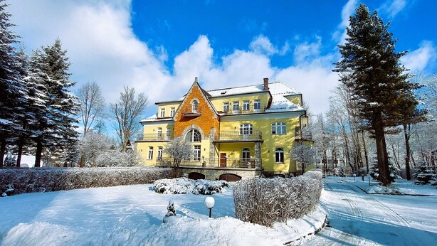A large, two-story building with a prominent tower and multiple balconies, surrounded by snow-covered trees and a clear sky. - Pensjonat Halny (Zakopane)