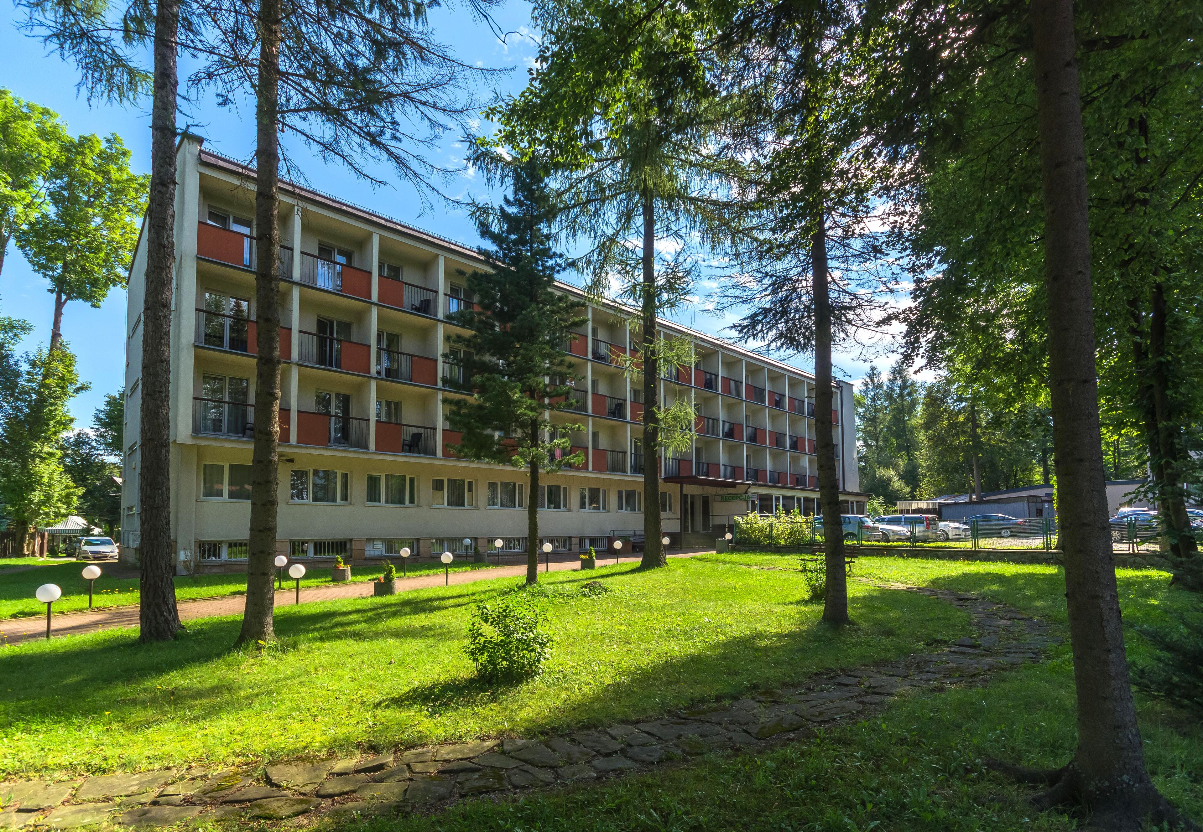 Een hotel met meerdere verdiepingen en balkons, omringd door bomen en een verzorgd gazon.