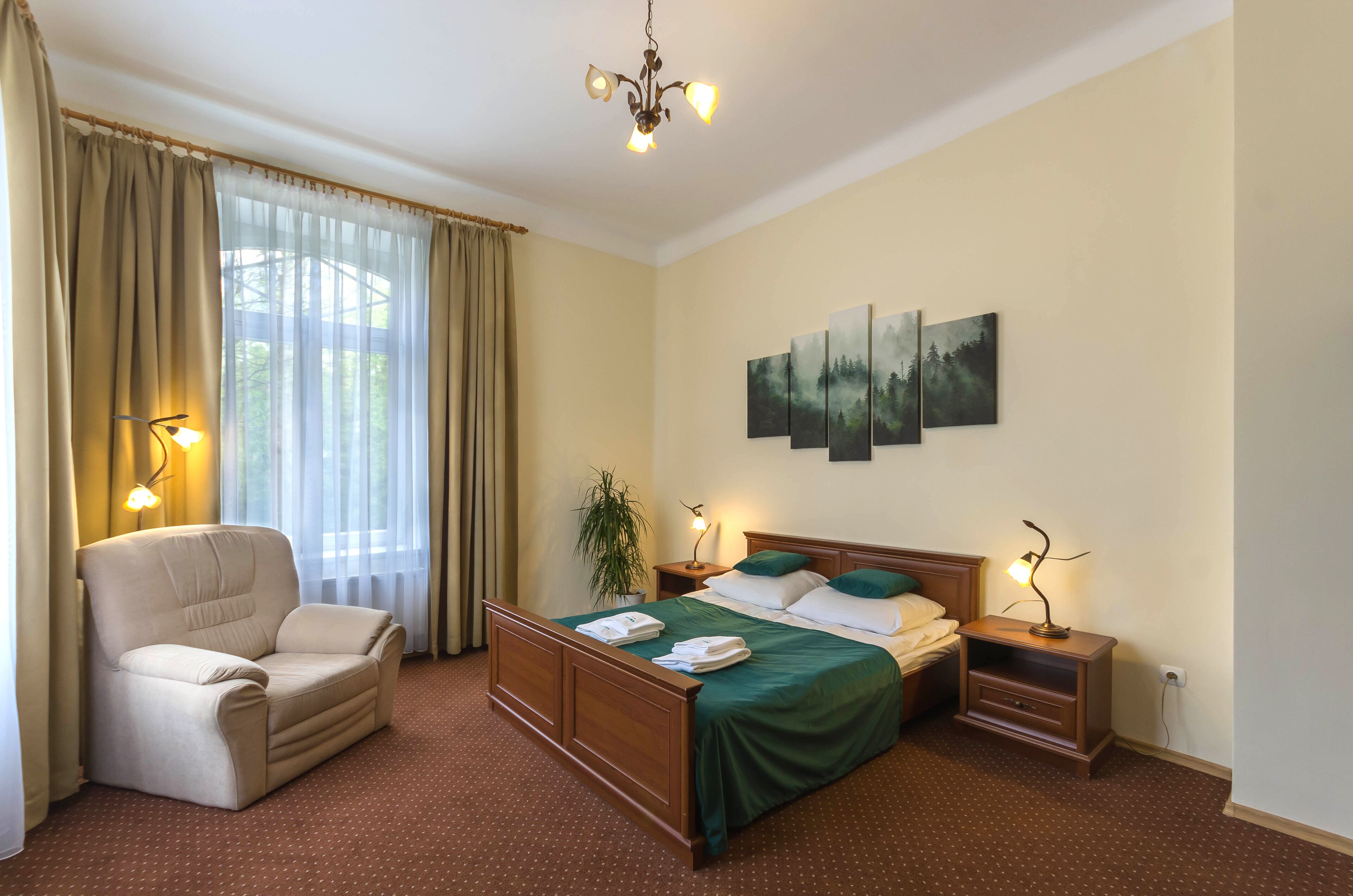 Une chambre d’hôtel avec un lit, une chaise, une table de chevet, une lampe et un tableau au mur.