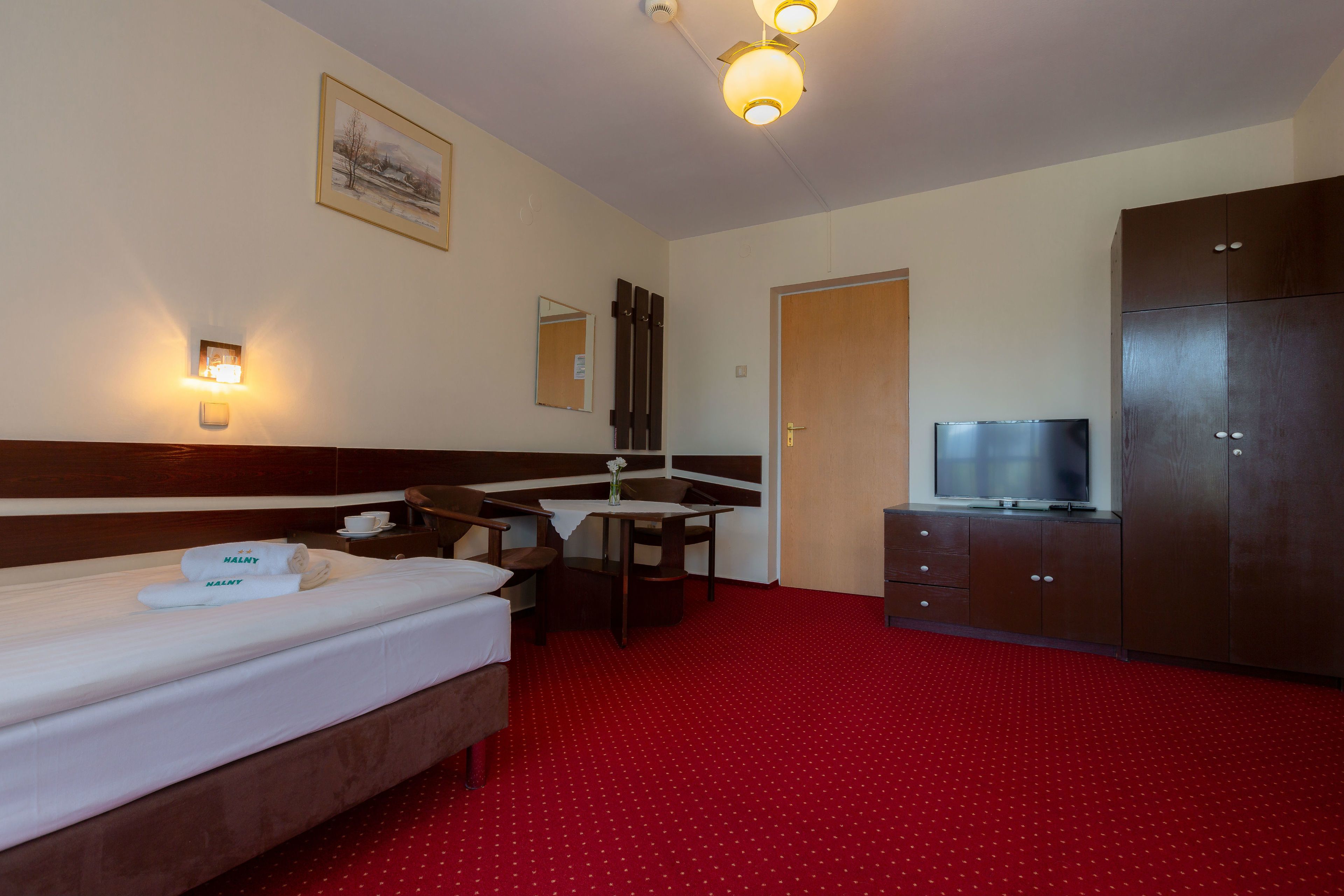 Una camera d'albergo con un letto, una scrivania con sedia, una televisione e un armadio.