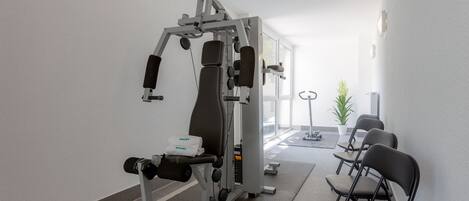 A gym with exercise equipment, a seating area with chairs, and a potted plant.
